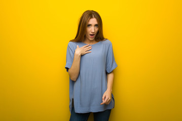 Young redhead girl over yellow wall background surprised and shocked while looking right