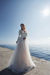 Fototapeta na wymiar Bride in a wedding dress on the beach by the sea against the background of a blue sky