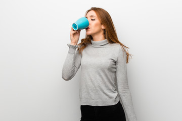 Redhead girl over white wall holding a hot cup of coffee