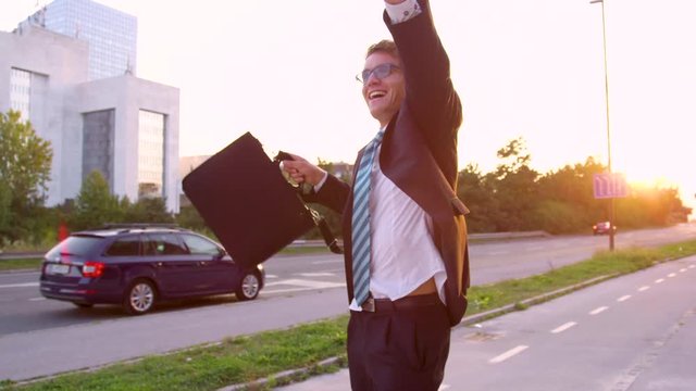 SLOW MOTION, SUN FLARE, CLOSE UP: Excited Caucasian yuppie dancing down the sunlit street after getting promoted. Happy businessman dances along the empty sidewalk on a beautiful summer evening.