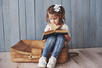 Ready to big travel. Happy little girl reading interesting book carrying a big briefcase. Freedom...