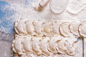 Dumplings on wooden board on blue table sprinkled with flour