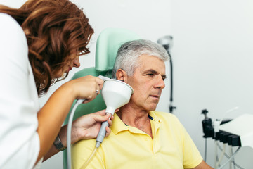 Senior man at medical examination or checkup in otolaryngologist's office. Ear irrigation and...