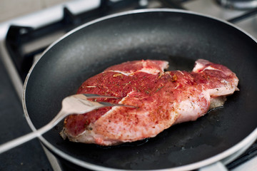 Raw pork chop in a frying pan with rosemary, pepper and salt.