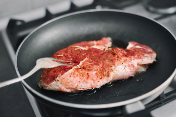 Raw pork chop in a frying pan with rosemary, pepper and salt.