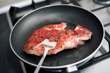 Raw pork chop in a frying pan with rosemary, pepper and salt.
