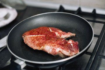 Raw pork chop in a frying pan with rosemary, pepper and salt.