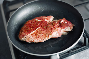 Raw pork chop in a frying pan with rosemary, pepper and salt.