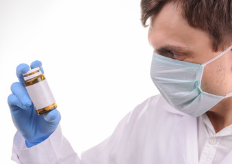 a doctor with mask in a white uniform looking at a bottle with pills that he is holding in his hand in a blue glove