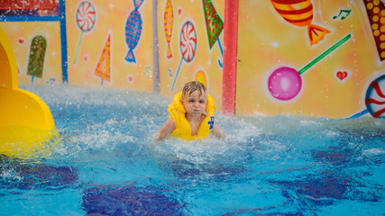 Obraz na płótnie Canvas a 6-year blond boy in a life vest jumping in the swimming pool of a hotel in Turkey