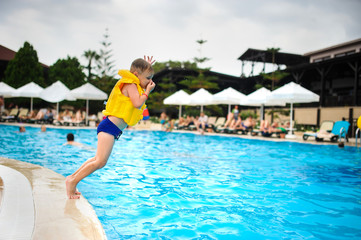 a 6-year blond boy in a life vest jumping in the swimming pool of a hotel in Turkey