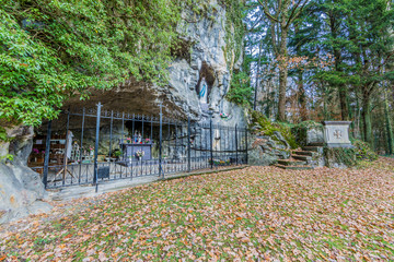 Beautiful replica of the Virgin of Lourdes in a natural grotto with a metal fence and a stone...
