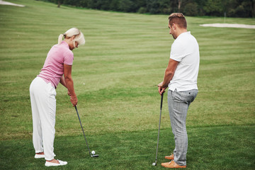 Girl playing golf and hitting by putter on green. Her teacher helps to explore the technique and make her first strikes