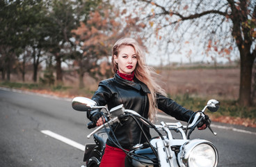 Obraz na płótnie Canvas A stylish biker woman posing outdoor with motorcycle. 