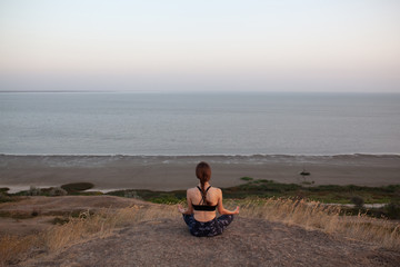 Naklejka na ściany i meble Anonymous young girl Practicing Yoga in Lotus pose sitting on the edge of rock against of see. Padmasana