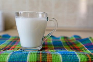 glass of milk is on the kitchen table on a multi-colored towel.