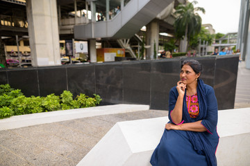 Mature beautiful Indian woman sitting and thinking in city