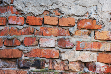 An old red brick wall, with peeling plaster and a covered stone.