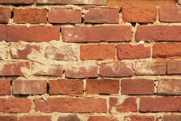 An old red brick wall, with peeling plaster and a covered stone.