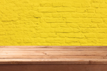 Empty wooden table over yellow brick stone wall background.