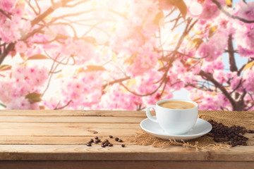 Coffee cup with coffee beans on wooden table over blossom cherry tree blurred background with copy space.
