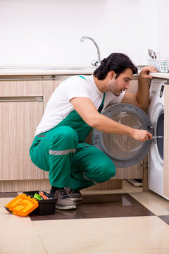 Young contractor repairing washing machine in kitchen