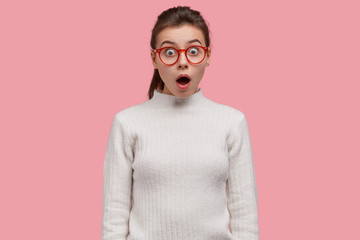 Young teenager stands in stupor at shocking scene, wears spectacles and casual outfit, being...