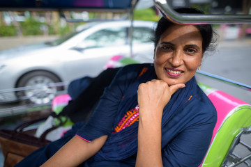 Mature beautiful Indian woman sitting and smiling in tuk tuk