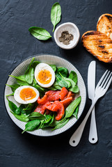 Delicious brunch - spinach, smoked salmon, soft boiled egg on a dark background, top view. Healthy eating diet concept