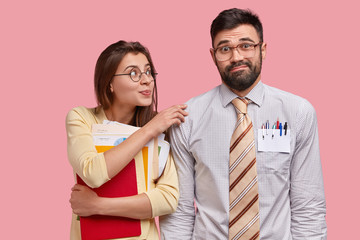Puzzled bearded guy in formal clothes listens advice from groupmate, holds notepad, keeps hand on shoulder of friend, collaborate together, pose against pink background. Collaboration concept