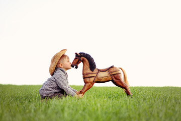 A boy, three years old, playing his toy rocking horse, dreaming about a real horse. a concept of true friendship and selfless love. Happy childhood in the countryside, the child takes care his pet.