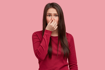 Photo of displeased woman closes nose with reek, feels terrible smell from garbage, wears red...