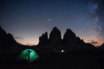 Little fog over the rocks. Two lighting tents with tourists inside near the Tre Cime three peaks mountains at night time