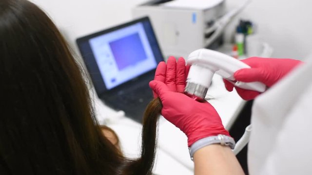 doctor dermatologist diagnoses the structure of the hair of a young pretty girl with a special tool - a trichoscope. Trichology, trichogram