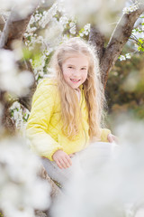 Fototapeta na wymiar Adorable little girl in blooming cherry tree garden