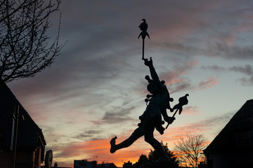 silhouette of court jester or imp toy dancing over rooftops - obrazy, fototapety, plakaty