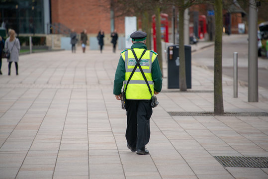 traffic warden civil enforcement officer wearing reflective yellow vest walks down the middle of the street completely alone