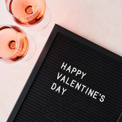 Valentine's day. Black letterboard with quote Happy Valentine's Day, and glass of rose wine on pink...