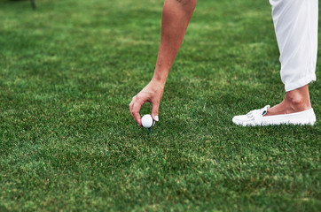 Sport and hobby conception. Female hand putting golf ball on the pin standing in the green field