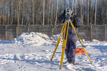 Surveyor conducts a topographical survey for the cadastre at a construction site in winter