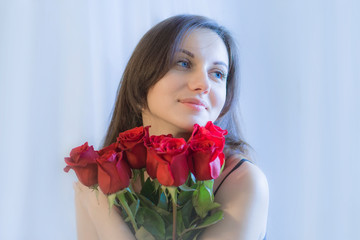 Romantic portrait of beautiful attractive young woman with a bouquet of red roses. Blue toned image