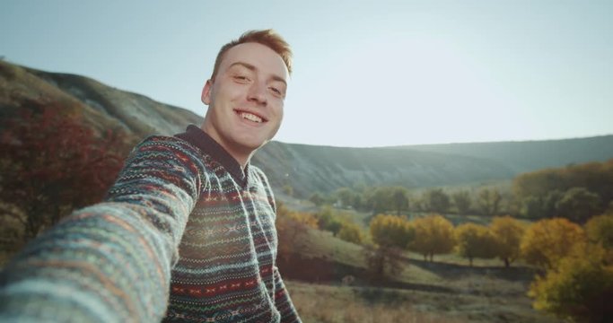 Large smiling redhead guy filming his self on nature taking a selfie video.