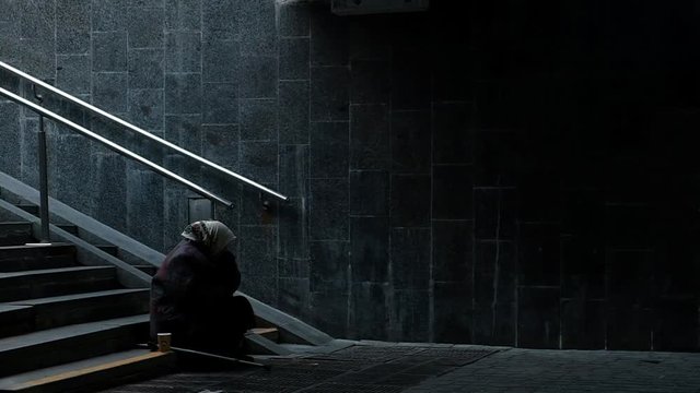 People passing by poor elderly woman that beggs in underground subway