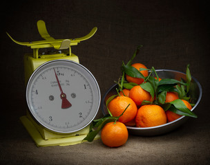 Oranges, tangerines on scales on rustic hessian. Dark, chiaroscuro style still life. Vintage theme.