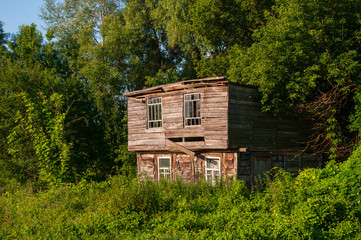 Obraz premium Light blue sky in the warm summer over the old abondoned house built from wood far away in the forest. Green trees near. Travelling on the suburb roads 