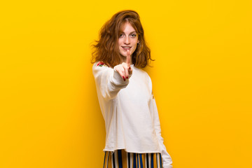 Young redhead woman over yellow wall showing and lifting a finger