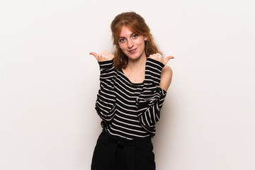 Young redhead woman over white wall giving a thumbs up gesture with both hands and smiling