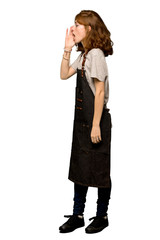 A full-length shot of a Young redhead woman with apron shouting with mouth wide open to the lateral over isolated white background