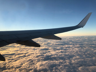 Obraz premium Aeroplane wing taken looking outside and Aeroplane window showing clouds and the Sunsetting in the background.