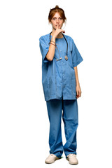 A full-length shot of a Young redhead nurse showing a sign of silence gesture putting finger in mouth over isolated white background